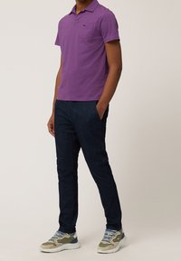 Fialové polo tričko s krátkým rukávem a náprsní kapsou, spárované s tmavě modrými slim-fit džíny a vícolorovými sportovními botami.