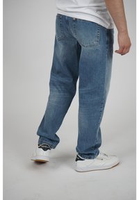 Vaaleansiniset farkut rentoilla mitoituksilla, näkyvällä tikkauksella ja kahdella takataskulla, yhdistettyinä valkoisiin Reebok-tennareihin.