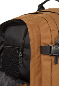 Bruine stoffen rugzak met zwarte voering, met een mesh zak, een interne ritszak en verstelbare straps. De hardware omvat een clipsluiting.