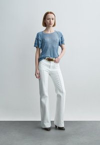 Haut en maille côtelée bleu clair avec manches à volants, associé à un pantalon blanc évasé taille haute et une ceinture marron. Texture lisse et coupe ajustée.