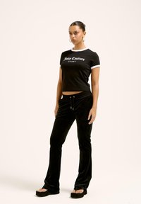 Černý zkrácený tričko má bílý lem a nápis "Juicy Couture Sport". Měkké černé sametové kalhoty s elastickým pasem a rozšířenými nohavicemi.