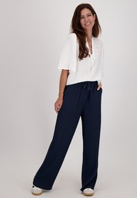 Witte blouse met korte mouwen en een strikdetail bij de halslijn, gecombineerd met marineblauwe wijde broek met een gevoeld patroon.