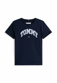 Marineblå bomulds T-shirt med korte ærmer, med "TOMMY" i hvide bogstaver i en buet skrifttype og en lille logo detalje nederst.