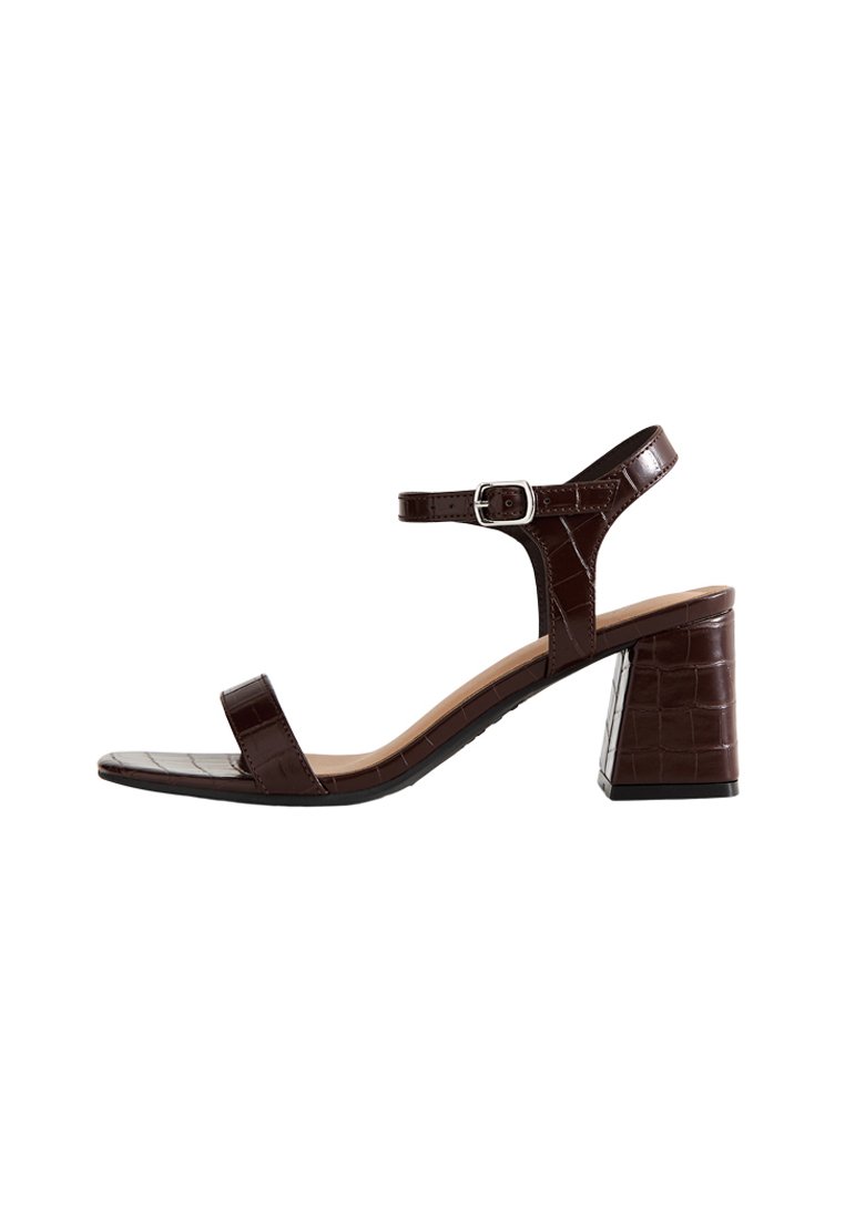 Sandal de tacón bloque de cuero marrón con tira en el tobillo y hebilla plateada, que presenta un patrón de cocodrilo texturizado y un diseño de punta abierta.