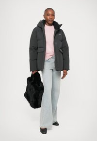 Zwarte pufferjack met een capuchon en zakken aan de voorkant, gecombineerd met een lichtroze sweater, flare lichtblauwe jeans en een zwarte fauxbont tas.