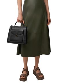 Zwarte leren handtas met een bovenhandvat, een zak met klep aan de voorkant en gouden hardware. Draag het met een groene leren rok en bruine plateau-sandalen.