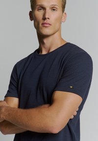 Navy blauwe T-shirt met korte mouwen, voorzien van een ribbelstructuur en een klein logo-accent op de linker mouw. Ronde halslijn en een ontspannen pasvorm.