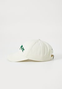 Cotton baseball cap, off-white color, features green embroidered text on the front and side, adjustable strap at the back.