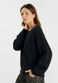 Maglione nero lavorato a maglia con un motivo testurizzato, maniche larghe e scollatura rotonda, abbinato a pantaloni con stampa leopardata.