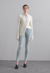 Langermet, plissert elfenbensfarget bluse parret med lyseblå skinny jeans. Sammen med svarte, spisse sko. Minimalistisk, moderne stil.