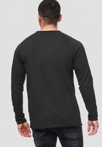 Camisa negra de manga larga con mangas raglán, hecha de un tejido suave. Presenta un escote redondo y un diseño liso, vista desde la parte de atrás.