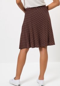 Jupe brune à motifs géométriques, coupe évasée, taille élastique, longueur au genou, portée avec des chaussures blanches.