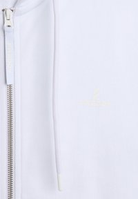 Hoodie zippé blanc avec une fermeture éclair à l'avant, texture côtelée et logo brodé discret. Comprend un cordon de serrage avec un embout en plastique.