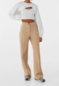 Vit kort sweatshirt med nyckelhålsdesign, matchad med beige vida byxor som har knäppning fram. Bärs med grå sneakers.