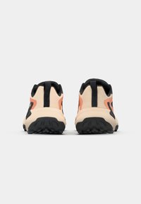 Sneakers med en beige overdel, svarte detaljer og en teksturert svart såle. Har en uttalt hæl og en bakre pull-tab for enkel påkledning.