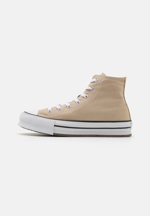 Høye kanvas sneakers i lys beige med hvite snørebånd, gummitåhette, svart-hvite stripete såle og et teksturert tekstiloverdel.