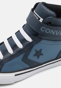 Hoge sneakers met een donkerblauwe leren bovenkant, witte veters en een zwarte rubberen zool met een gestikt sterlogo detail.