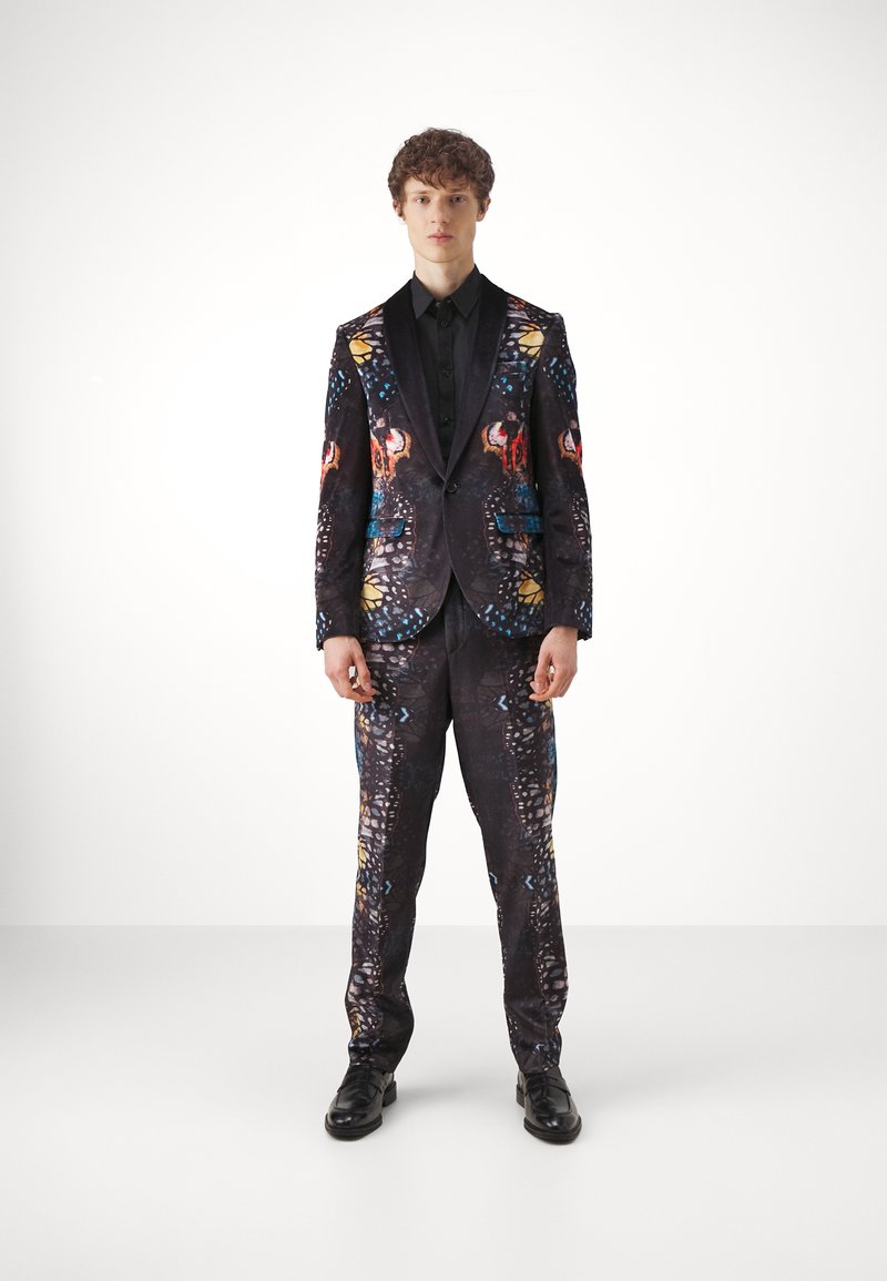 Black suit with colorful floral and abstract patterns, featuring a notched lapel and slim fit trousers. Paired with a black shirt and shoes.