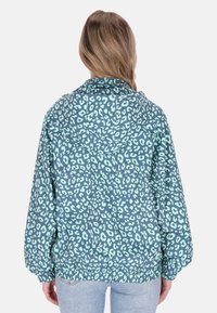 Sudadera con capucha de tela azul con estampado de leopardo en verde menta. Puños y bajo elásticos con un ajuste holgado. Vista desde atrás.