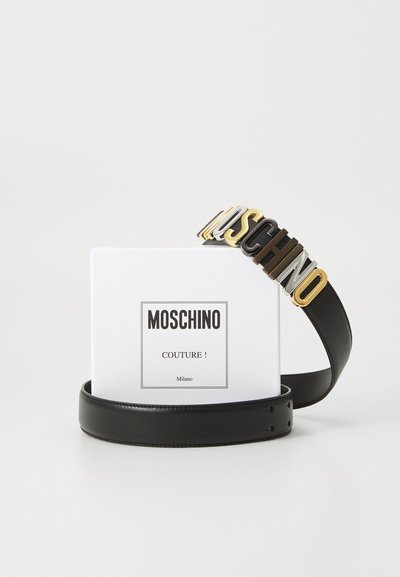 Fekete bőr öv, amelyet egy többszínű Moschino logó csat díszít, mellette egy fehér termékdoboz Moschino Couture! márkázással.