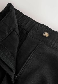 Schwarze Hose mit teilweise offenem Reißverschluss, Knopfverschluss und elastischem Bund auf hellem Hintergrund.