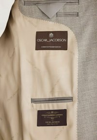Interno di giacca grigia con fodera crema, presenta etichette Oscar Jacobson e Vitale Barberis Canonico, tasca con bordatura grigia, cuciture ordinate.