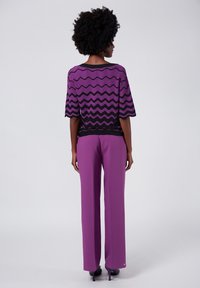 Lila och svart zigzag-mönstrad topp med korta ärmar, tillsammans med högmidjade lila byxor. Sval textur och avslappnad passform.
