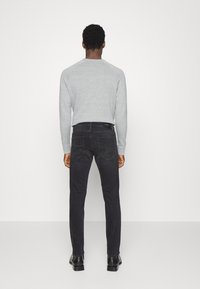 Jeans negro de mezclilla con corte ajustado, combinados con un suéter gris claro. Detalle de los bolsillos traseros visibles, textura suave y diseño de pierna recta.