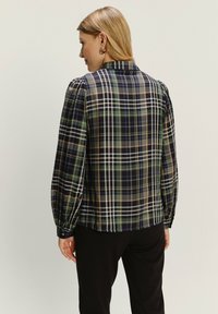 Karirana košulja u tamnoplavoj, zelenoj i bež boji s dugim napučenim rukavima, ovratnikom i dugmadi na manžetama. Prozirna, lagana tkanina.