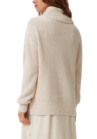 Cremfarbener Strickpullover mit hohem Kragen, gerippter Textur und Fallansatzschultern. Hat eine lockere Passform und gefütterte Ärmel.