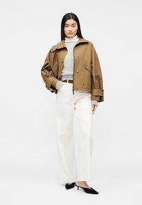 Γυναίκα που φοράει καφέ κοντή ζακέτα πάνω από γκρι ζιβάγκο, λευκό παντελόνι φαρδύ και μαύρα παπούτσια με μυτερό τακούνι kitten.