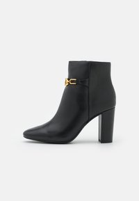 Svart läderankleboot med spetsig tå, en medelhög klack i blockform och en guldfärgad spänne på sidan. Slät textur, inga mönster.