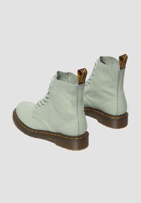 Botas de tobillo de cuero verde menta con diseño de cordones, detalle de costura amarilla y suela marrón. Cuenta con una pestaña en la parte posterior.
