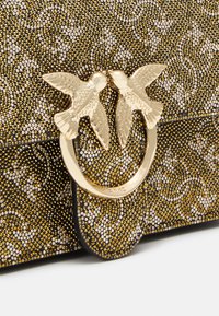 Borsa a pochette oro e nera con un intricato motivo in perline, caratterizzata da un prominente motivo di due uccelli in oro come accessorio e un accento ad anello circolare.