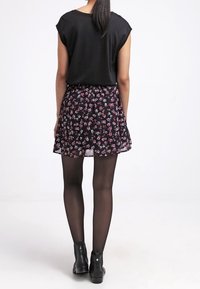 Blouse noire à manches courtes associée à une jupe noire à fleurs. La jupe présente une coupe évasée avec des fleurs roses et blanches, portée avec des bottines noires.