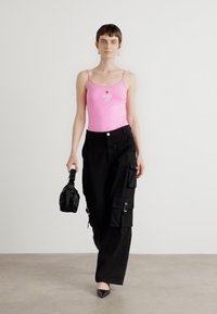 Rosa tettsittende tank topp med tynne stropper, svarte cargo-bukser med flere lommer og en liten svart håndveske. Spisse svarte hæler.
