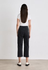 Zwarte corduroy cropped broek met hoge taille en twee achterzakken, gecombineerd met een witte aansluitende t-shirt en crèmekleurige schoenen.