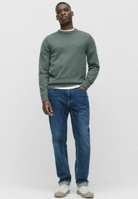 Vihreä neule pyöreällä kauluksella, ribbaatut hihansuut ja helma, yhdistettynä sinisiin farkkuihin ja vaaleisiin lenkkareihin. Yksinkertainen muotoilu, ei kuvioita.