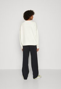 Hvit oversized hettegenser, avslappet passform med ribbet mansjetter. Kombinert med marineblå vide bukser og sporty sneakers. Glatt tekstur, minimalistisk design.