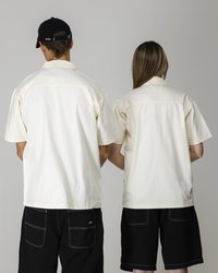 Short-sleeve, cream-colored shirts with a buttoned collar. Worn with black shorts featuring twin back pockets and light stitching.
