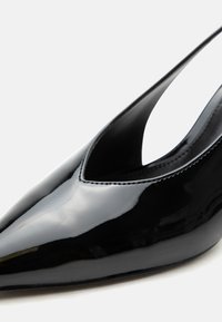 Γυαλιστερό μαύρο γοβάκι με μυτερή μύτη, λουράκι στο πίσω μέρος και λείο, λαμπερό φινίρισμα σε λευκό φόντο.