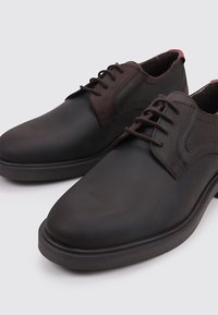 Zapatos de cuero negro con cordones, punta redondeada, detalles de costura sutil y una textura suave. Diseño minimalista con una suela oscura.