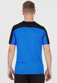 Blå och svart atletisk tröja med korta ärmar, som har en helblå kropp, svarta axlar och en slät textur.
