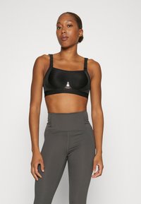 Reggiseno sportivo nero con spalline regolabili e finitura liscia. Presenta un piccolo logo al centro, abbinato a leggings grigi a vita alta.
