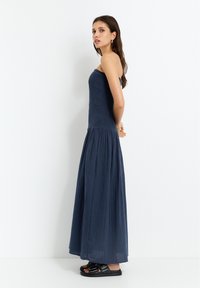 Navyblaues, trägerloses Maxikleid mit strukturiertem Oberteil und plissiertem Rock. Getragen mit schwarzen Sandalen. Einfaches, fließendes Design.