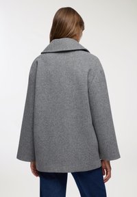 Szary wełniany płaszcz z szerokim kołnierzem, opuszczonymi ramionami i luźnym krojem. Teksturowana tkanina z subtelnym wzorem, rękawy do długości średniej i prosty krój.