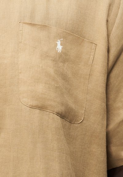 Beež linane särk rinnataskuga, kus on väike valge tikandiga hobuse seljas polo mängija logo.