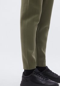 Pantalones de punto verdes con detalles acanalados a lo largo de los laterales, combinados con zapatillas negras de cuero con superficie texturizada y diseño de cordones.