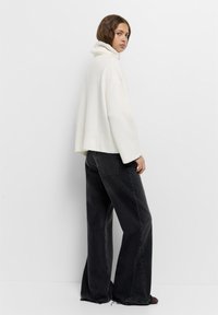 Ylihinnoiteltu valkoinen pooloneule, jossa on ribbireunat, yhdistettynä tummanharmaisiin leveälahkeisiin farkkuihin, joissa on kuluneet lahkeensuut.