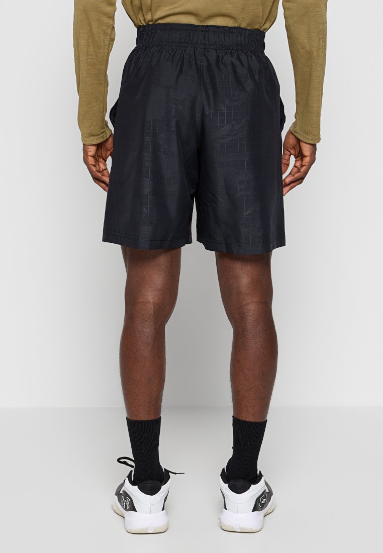 Shorts de sport noirs avec un motif texturé, taille élastique et poches latérales, associés à des chaussettes noires et des baskets blanches.